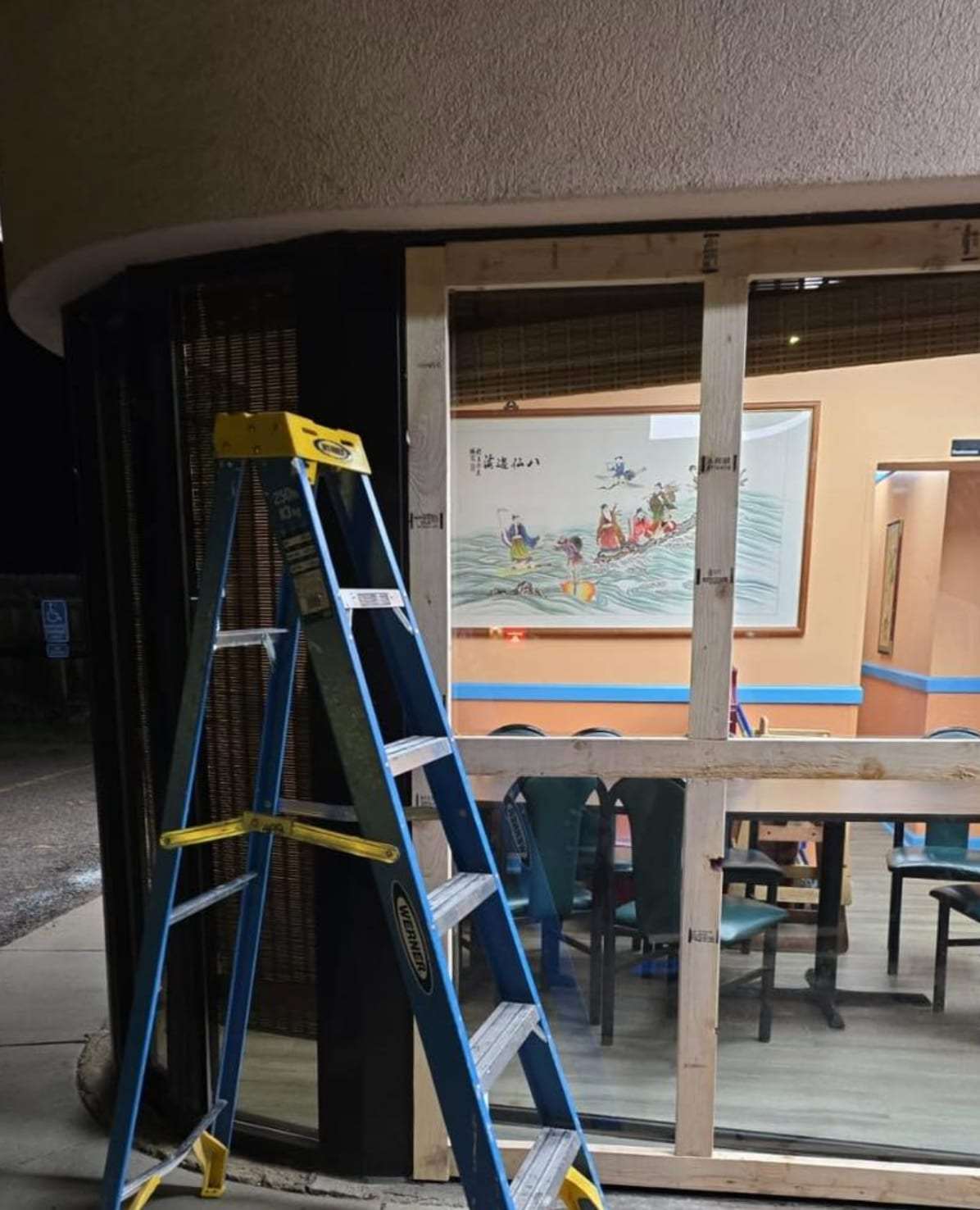 Boarded storefront window with a ladder after damage
