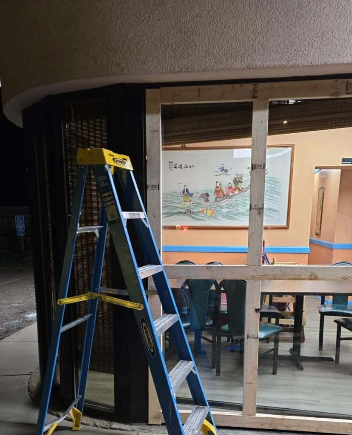 Boarded storefront window with a ladder after damage